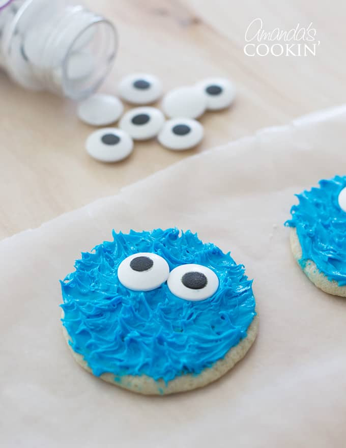 Close-up of a Cookie Monster cookie on parchment paper with candy eyes in the background, ready to be used.