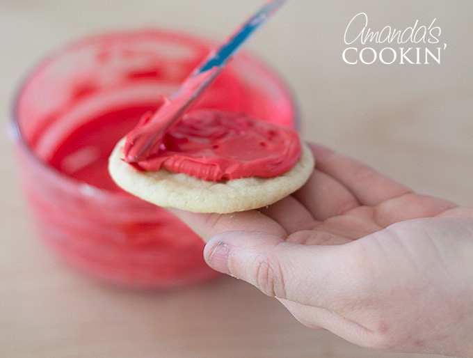 Close up image of spreading red frosting onto a sugar cookie to create Elmo.