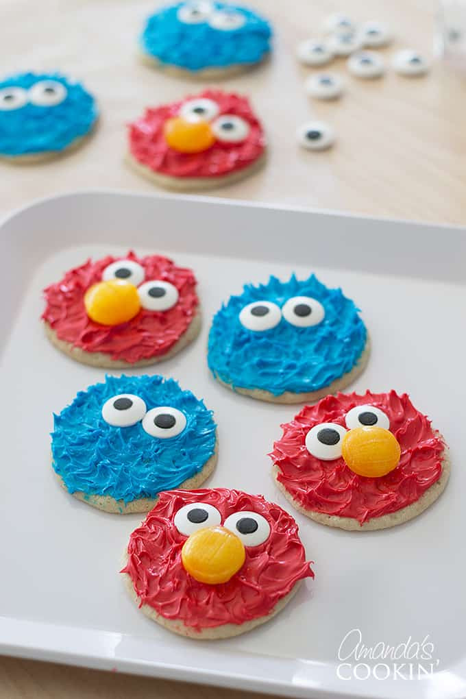 Close-up of Cookie Monster and Elmo cookies on a white plate, showcasing their fun textured frosting and candy eyes.
