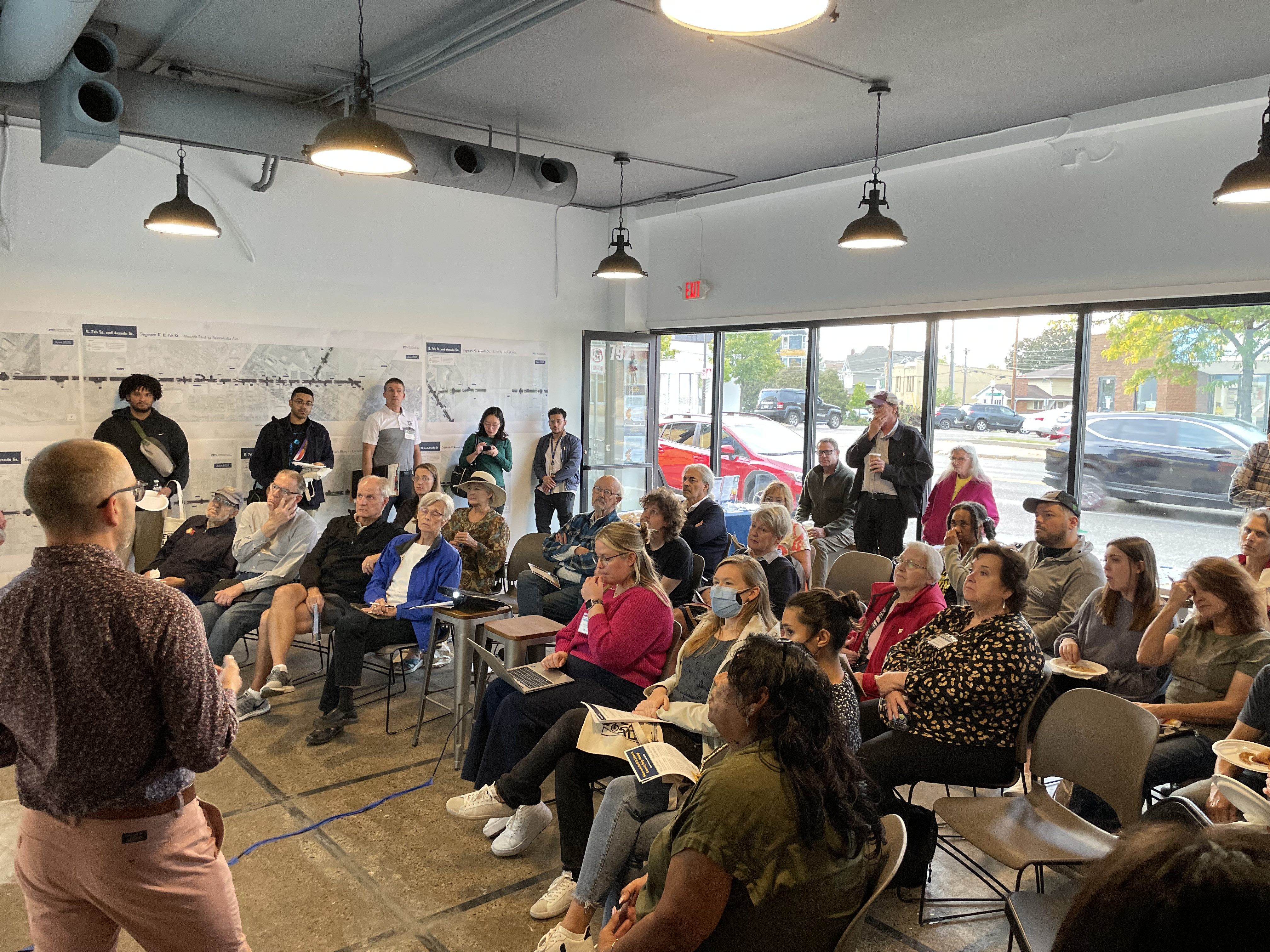 A Community Design Workshop session in progress, with community members listening to a presentation about the East 7th Street project.