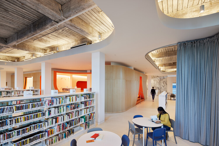 Bright and inviting interior space at Adams Street Library, equipped with bookshelves, tables, and contemporary lighting.