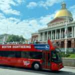 Boston Sightseeing double-decker bus tour passing by the Massachusetts State House, a landmark near Acorn Street in Beacon Hill, Boston.
