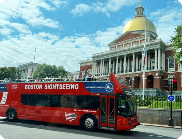 Boston Sightseeing double-decker bus tour passing by the Massachusetts State House, a landmark near Acorn Street in Beacon Hill, Boston.