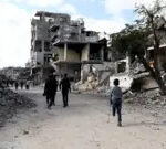 Reuters People, including a child on a crutch, missing the lower half of his left leg, walk past the grey, dusty rubble of houses and buildings destroyed during the war in Al-Bureij in central Gaza