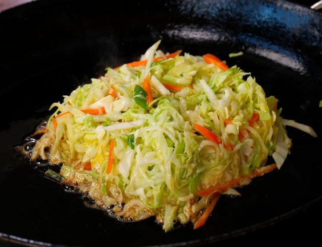 Cabbage and vegetable mixture being shaped into a patty in a skillet for Korean street toast.