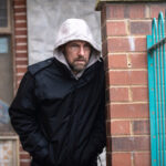 Rob looking disheveled and hiding by a wall