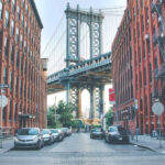 Manhattan Bridge view from Washington Street, framed by red brick buildings in Dumbo, Brooklyn, with cobblestone streets in the foreground