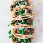 overhead view of carne asada mexican street tacos, in a double layer of crispy corn torillas and sprinkled with cilantro and onion.