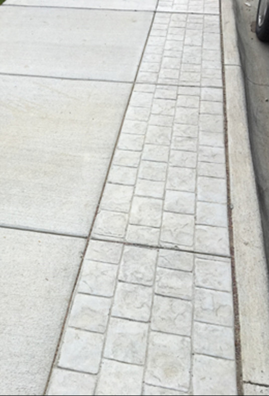 Sidewalk with decorative brick-like edging, representing a minimal maintenance approach.