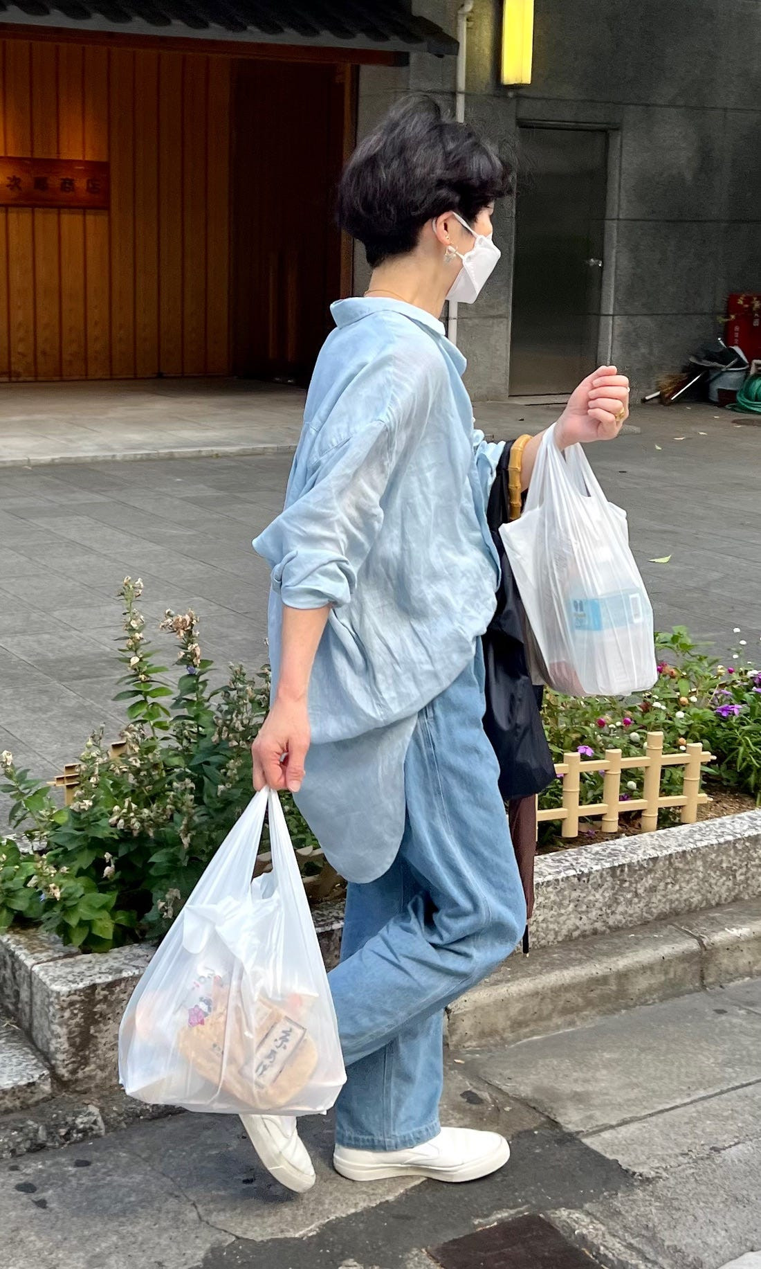 Street style photograph of a woman in a black dress and white cardigan, showing a classic and understated Japanese fashion look.