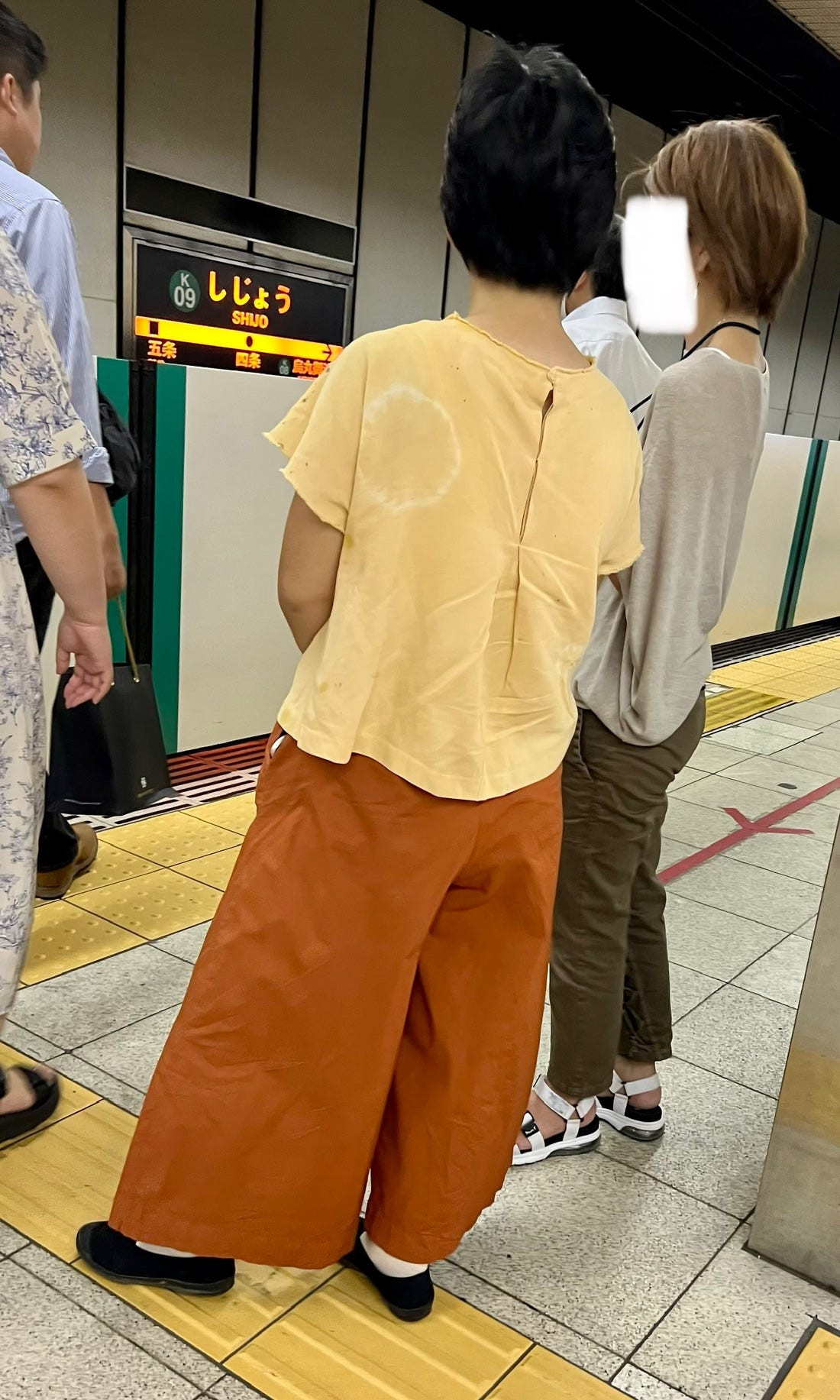 Street fashion photograph showcasing a person in layered, oversized clothing in neutral tones, typical of Japanese street style.