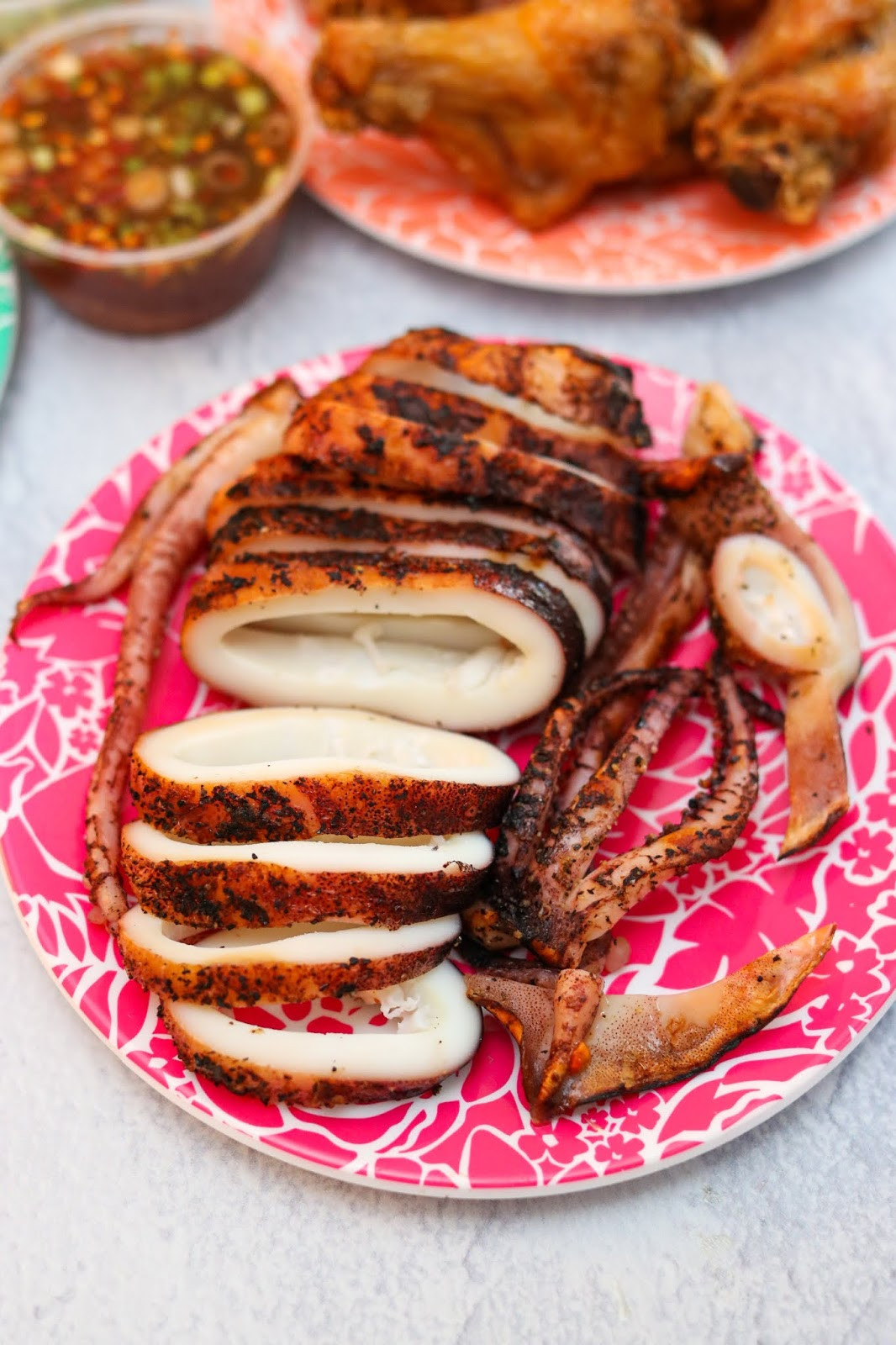 A close-up shot of perfectly grilled Pla Muk Yang, Thai grilled squid, drizzled with a vibrant spicy seafood sauce at JJ Thai Street Food restaurant.