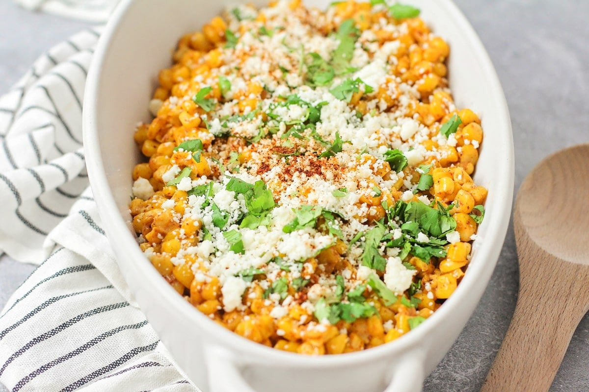 A close up shot of Mexican street corn served in a white bowl, garnished with fresh cilantro and cotija cheese, highlighting its inviting and flavorful appearance.