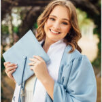 Smiling high school senior in graduation gown holding blue cap, Sabine Street Bridge Houston backdrop