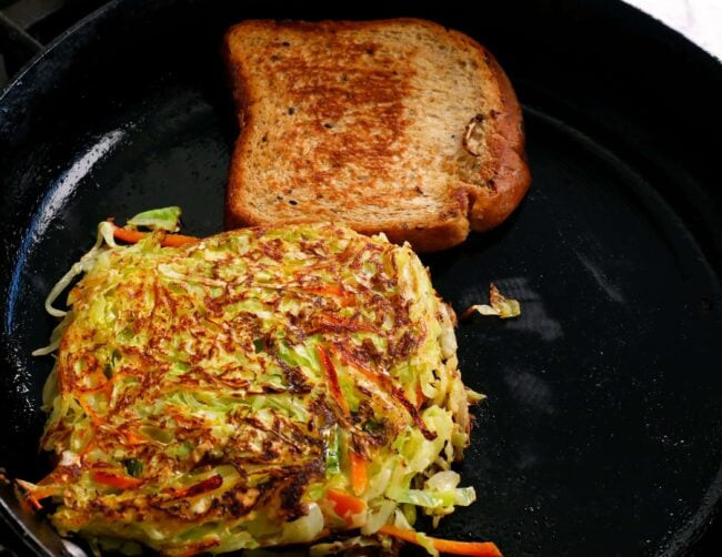 Cooking Korean street toast on a skillet with cabbage patty and toasted bread.