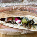 Tahini's O.G. Pita, a flavorful example of authentic Middle Eastern street food, featuring Syrian steak shawarma, fresh vegetables, and creamy tahini sauce.