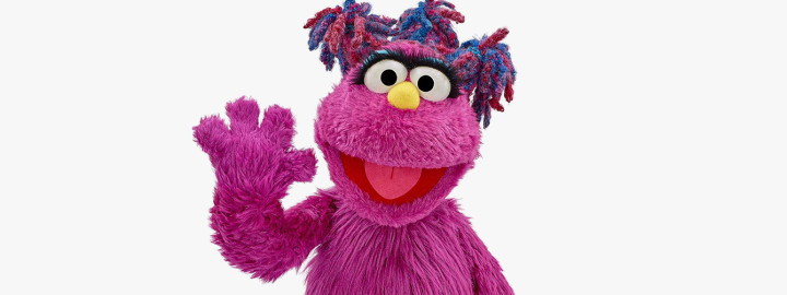 Zuzu Sesame Street South African Muppet character with arms crossed and smiling confidently